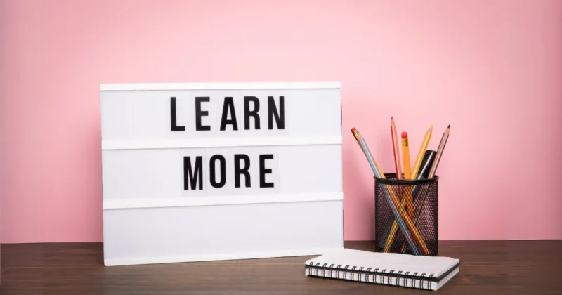 机のうえに置かれた鉛筆とメモ帳と「LEARN MORE」と書かれたパネル