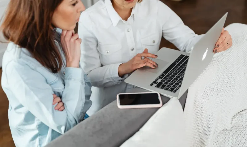 ノートパソコンとスマホを見ながら相談する2人の女性